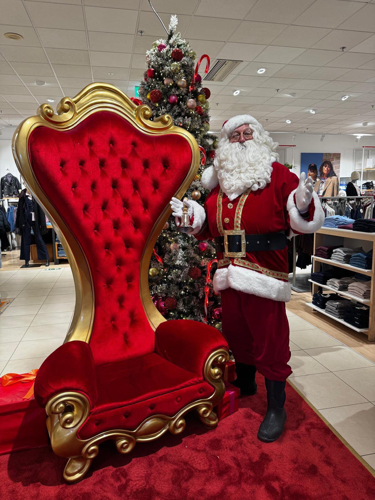 LE PÈRE NOËL debout près de son trône, clochette à la main